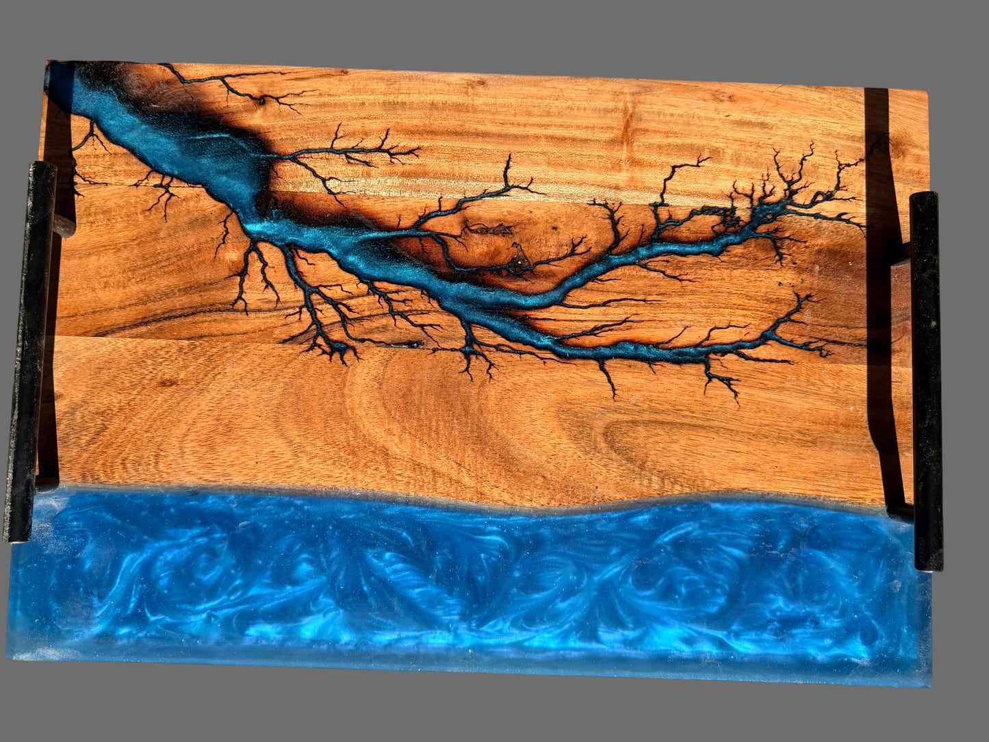 Premium resin board  with black metal side handles, featuring acacia wood grain with a sapphire blue resin fractal burning pattern and a thick blue resin base layer, shown on a plain gray background. Great birthday gift for her or him