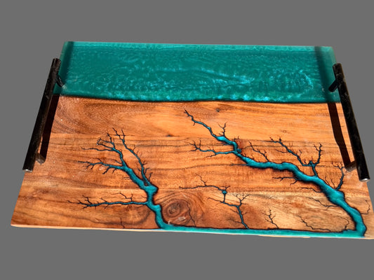 Premium resin board with black metal side handles, featuring a turquoise blue resin river pattern flowing across acacia wood grain surface, with a swirled turquoise resin top layer.