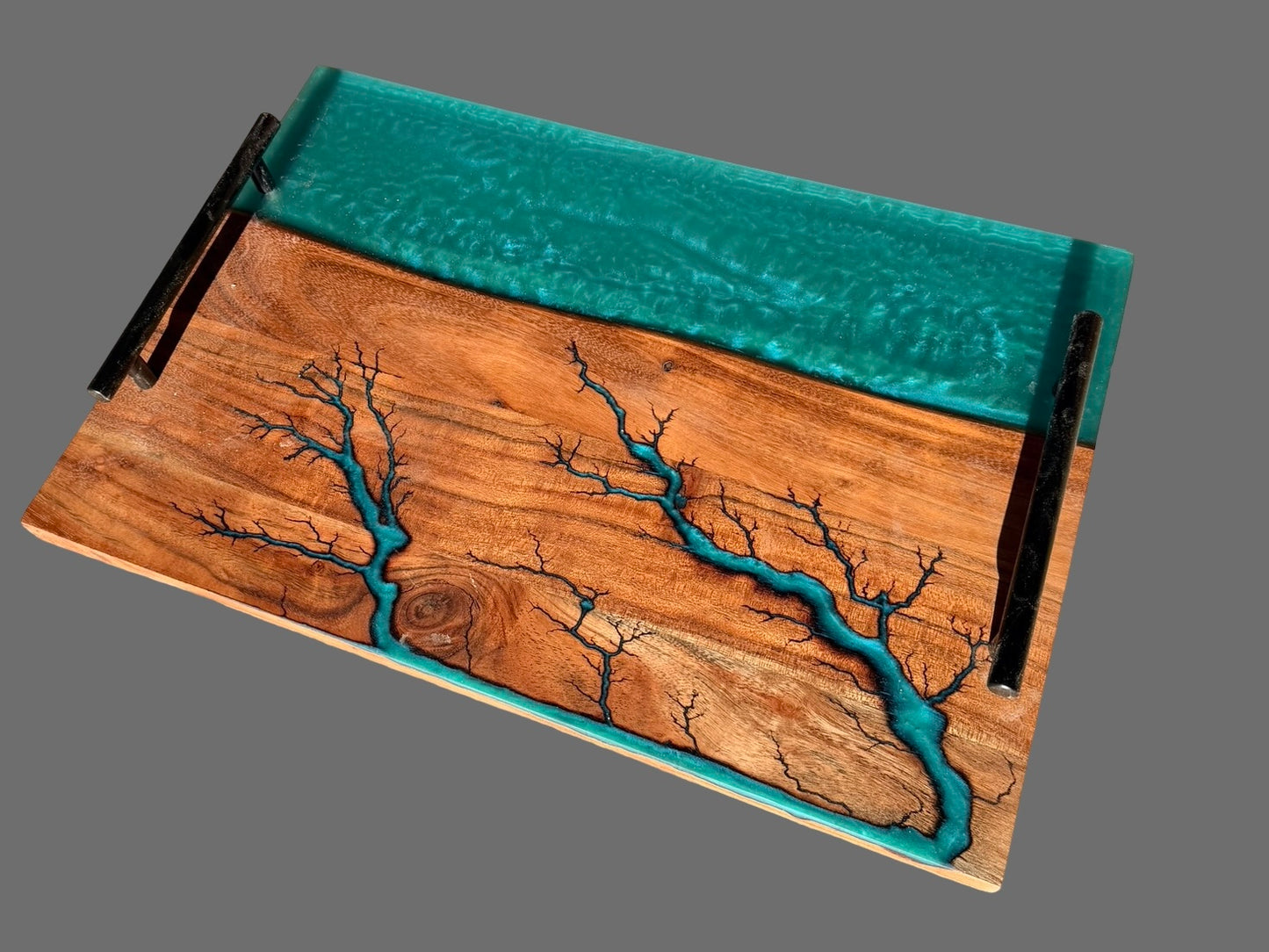 A rectangular serving board with black metal handles and a turquoise green resin inlay featuring a branching tree-like pattern, shown on a solid gray background. Made in Victoria, Australia 